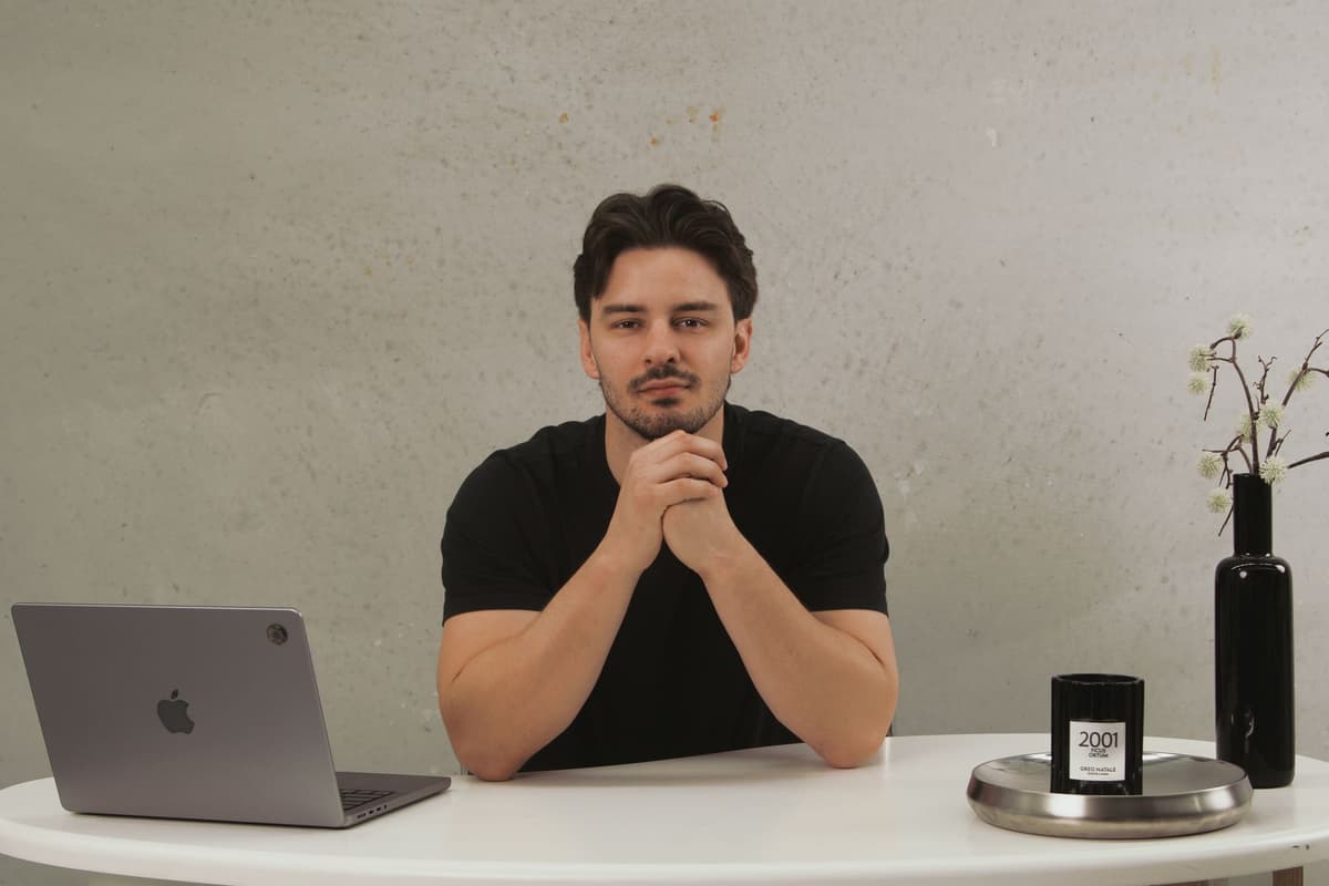 Luke Marinovic at a white desk with his hands clasped, looking at the camera, laptop open to one side.
