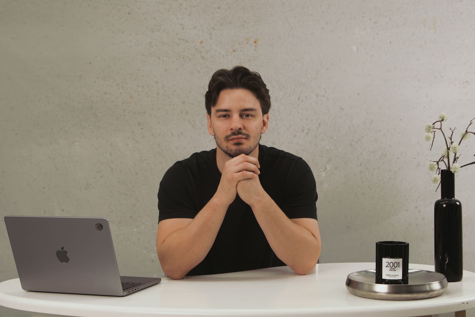 Luke Marinovic at a white desk with his hands clasped, looking at the camera, laptop open to one side.