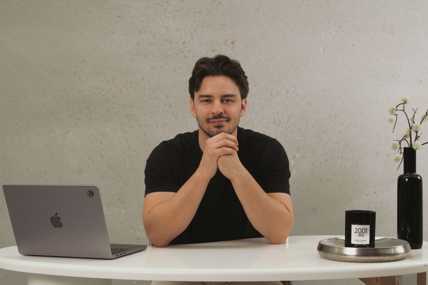 Luke Marinovic smiling at a white desk, hands clasped, laptop open beside him.