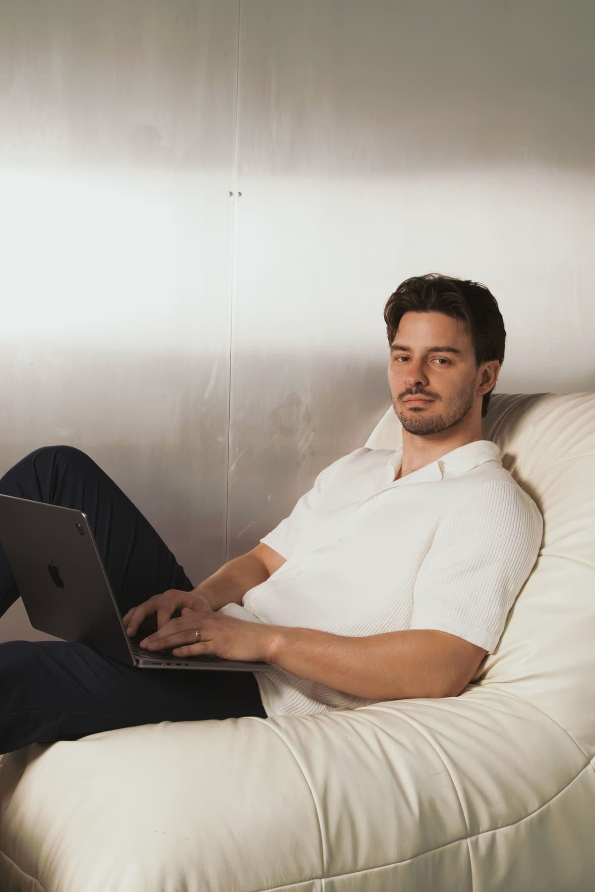 Luke Marinovic in a cream lounge chair with a laptop, looking at the camera.