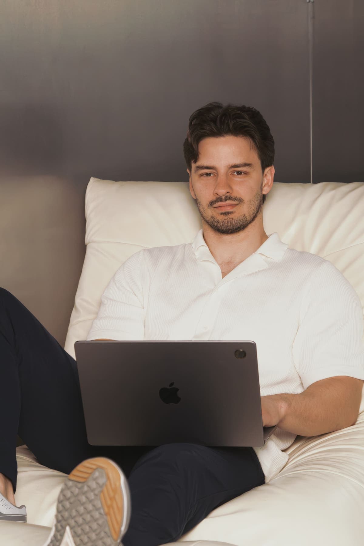 Luke Marinovic with a laptop on his lap in a cream lounge chair, looking at the camera.