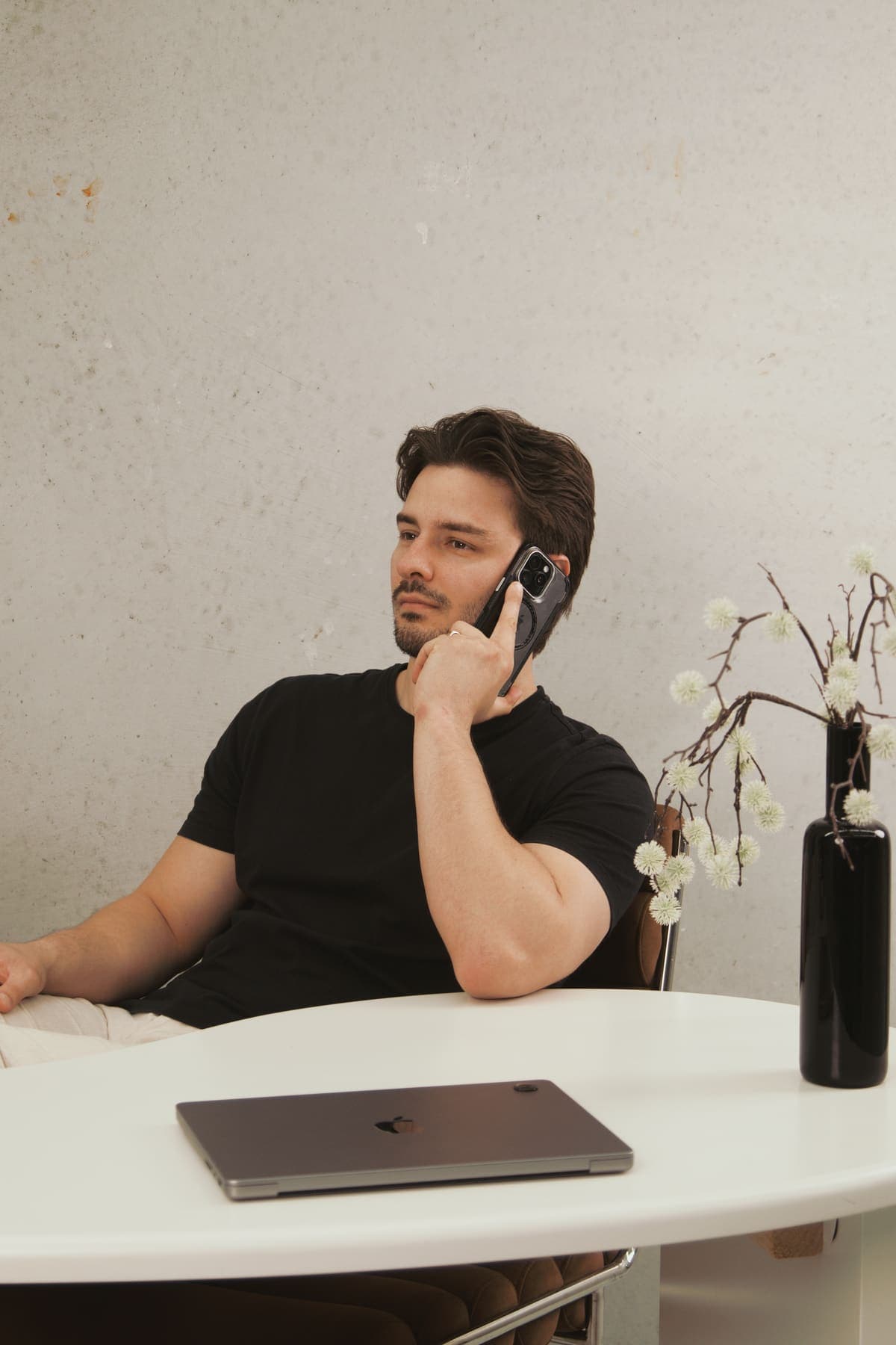 Luke Marinovic on a phone call at a round white desk, laptop closed in front of him, looking off to the side.