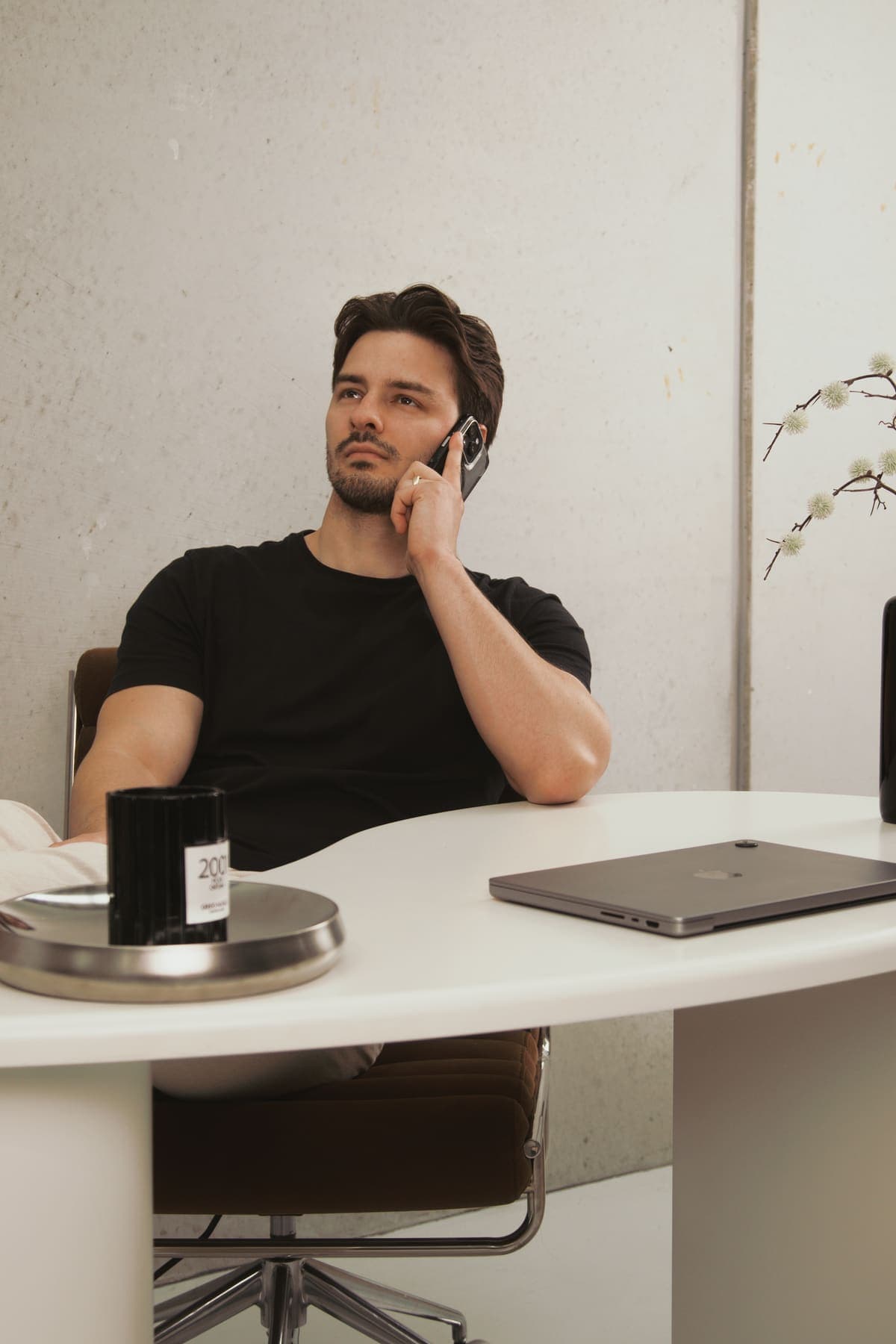 Luke Marinovic seated side-on at his desk, phone to his ear, mid-conversation, laptop open beside him.
