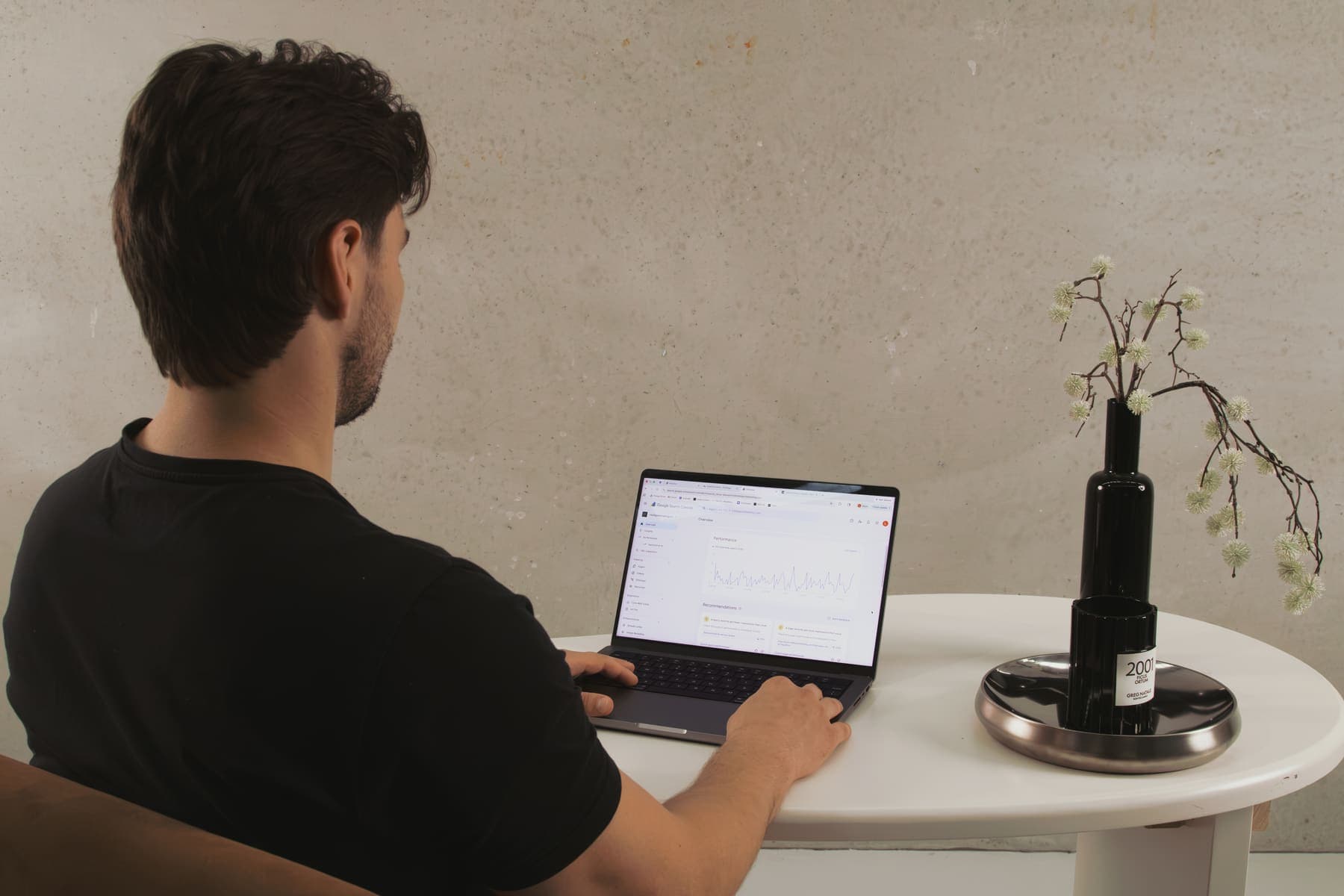 Luke Marinovic at a round white table, seen from behind, reviewing a search performance report on his laptop.