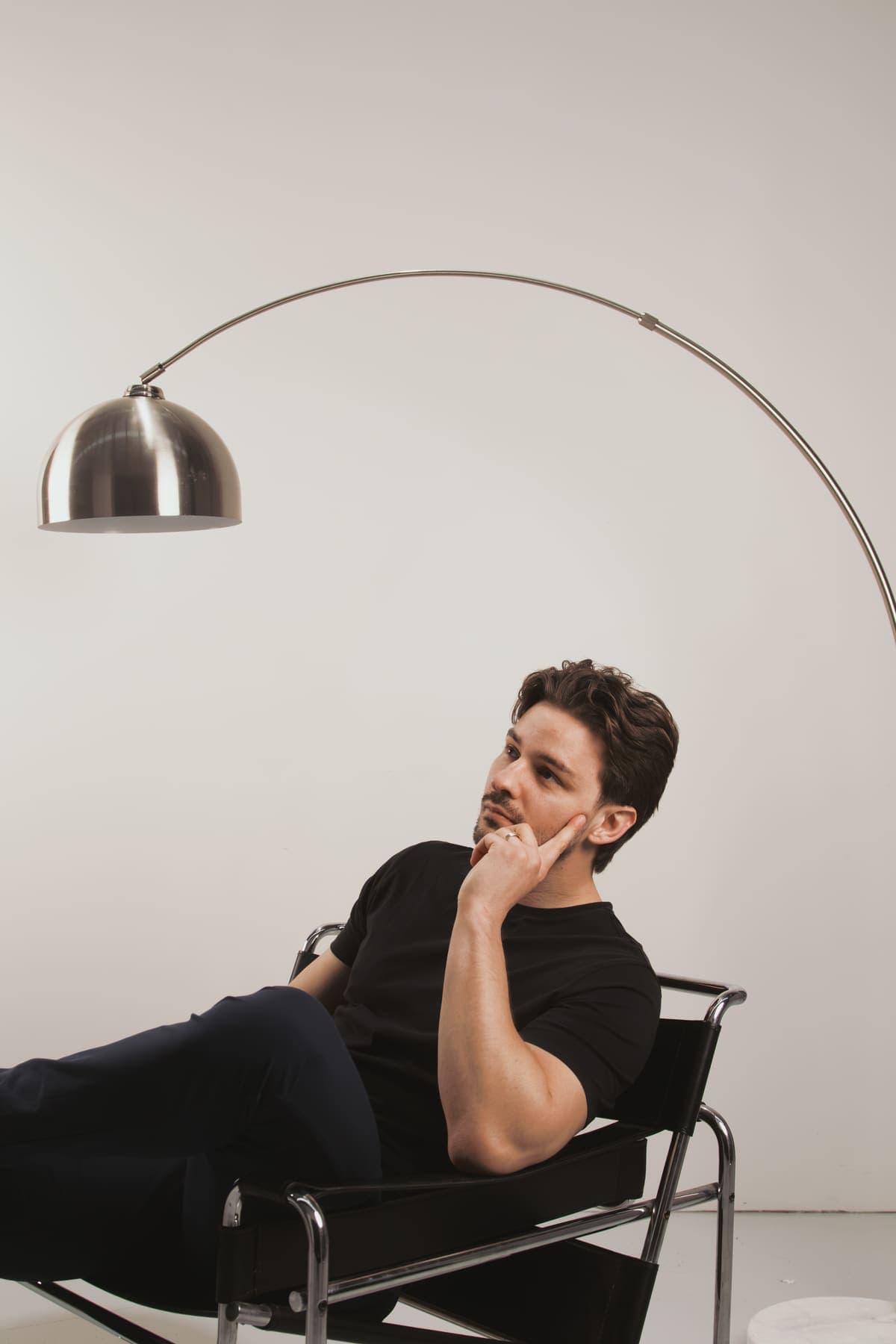Luke Marinovic in a sling chair with his hand on his chin, looking up, under an arc lamp.