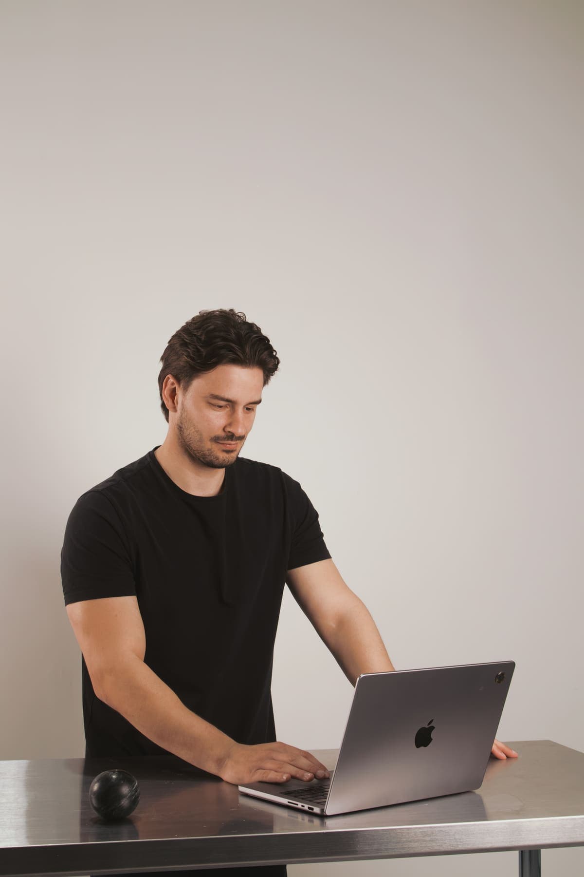 Luke Marinovic standing at a steel bench, typing on an open laptop.