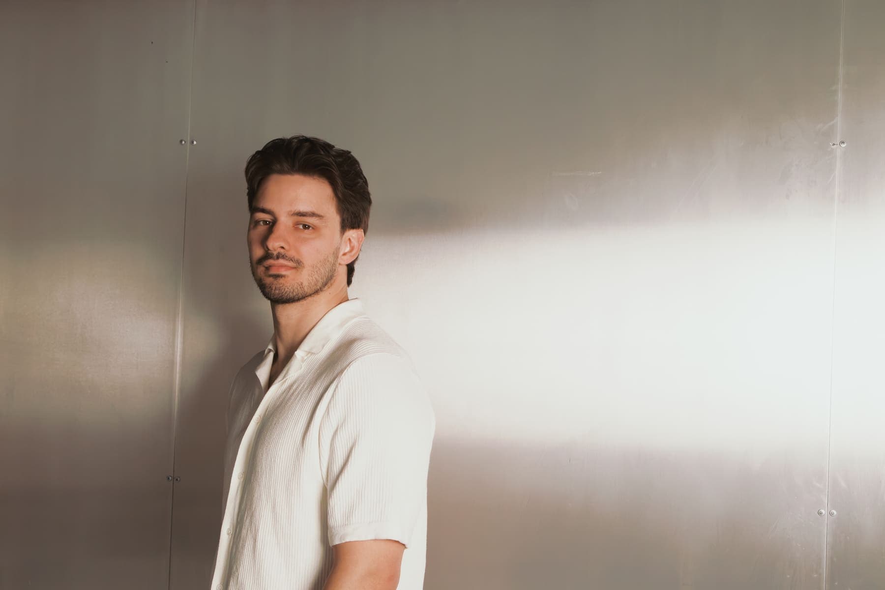 Luke Marinovic in a white shirt, shoulder to camera, a beam of light across a steel wall.